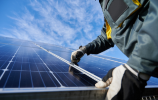 A person in protective gear is installing or inspecting solar panels under a clear blue sky.