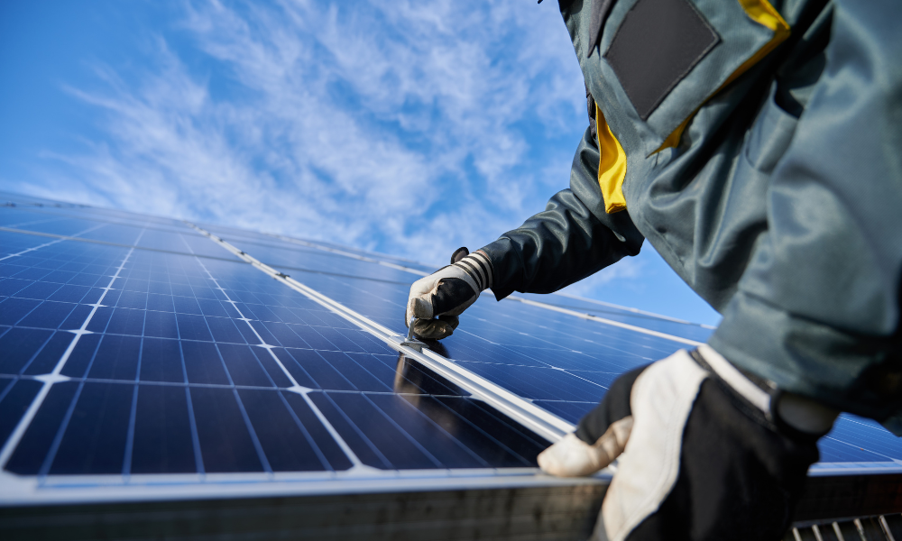 A person in protective gear is installing or inspecting solar panels under a clear blue sky.
